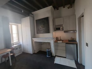 A compact kitchen with a microwave, sink, and a small refrigerator. There is a window providing natural light and a table with chairs. - Quiet Courtyard Apartment in Chartrons with Air Conditioning (Bordeaux)