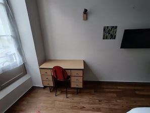 A room with a wooden floor, a desk with drawers, a red chair, a window with a sheer curtain, and a wall-mounted TV. - Apartment in mythical Chartrons floor 1 (Bordeaux)
