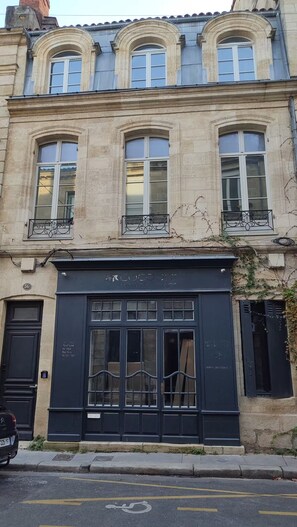 A building with three arched windows on the upper floor, a black storefront with signage, and a street in front. - Apartment in mythical Chartrons floor 1 (Bordeaux)