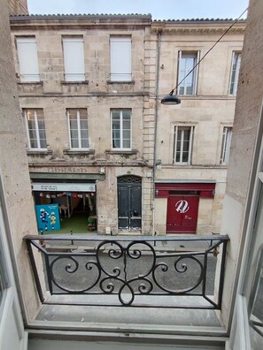 A view from a balcony with a wrought iron railing, overlooking a street with buildings, one with a red awning and another with a sign for a museum. - Apartment in mythical Chartrons floor 1 (Bordeaux)