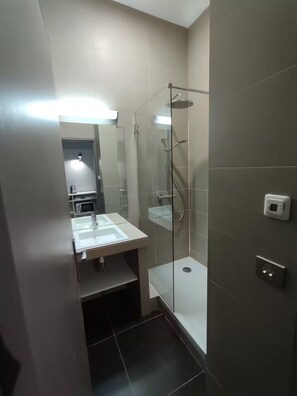 A modern bathroom with a glass-enclosed shower, a sink with a mirror, and a microwave on a countertop. - Apartment in mythical Chartrons floor 1 (Bordeaux)