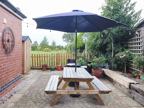 A wooden picnic table with a dark umbrella, surrounded by potted plants and a wooden fence. - The Snug (York)