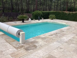 Ein rechteckiger Swimmingpool mit glasklarer, blauer Wasserfläche, umgeben von einer gefliesten Liegefläche.