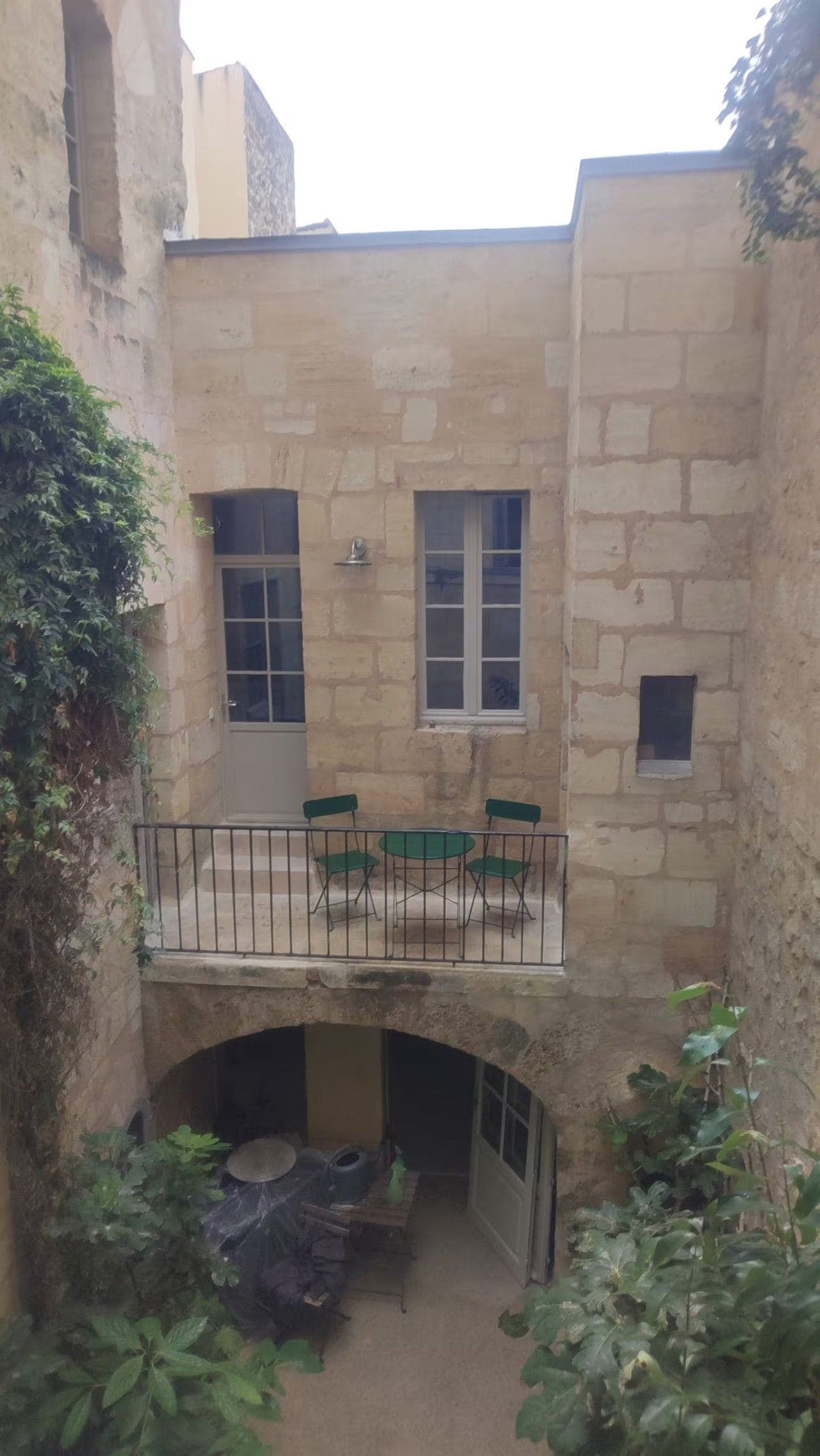 A stone building with a balcony, a small table with chairs, and a covered seating area.