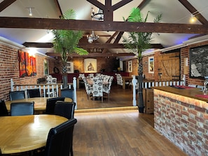 En restaurantindretning med murstensvægge, træbjælker og en bar.