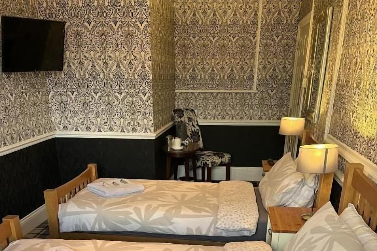 Et hotelværelse med to senge, et fjernsyn, et lille bord og tapet med et mønster.