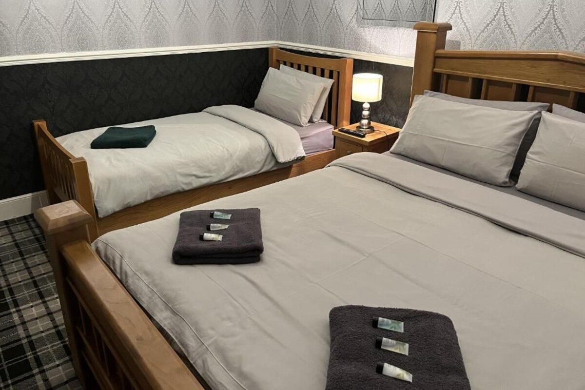 Et hotelværelse med to senge, et natbord med en lampe og tapet med et mønster.