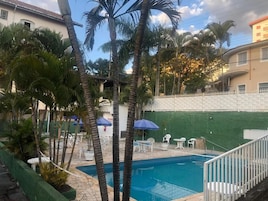 A swimming pool with a white fence, palm trees, and outdoor furniture.