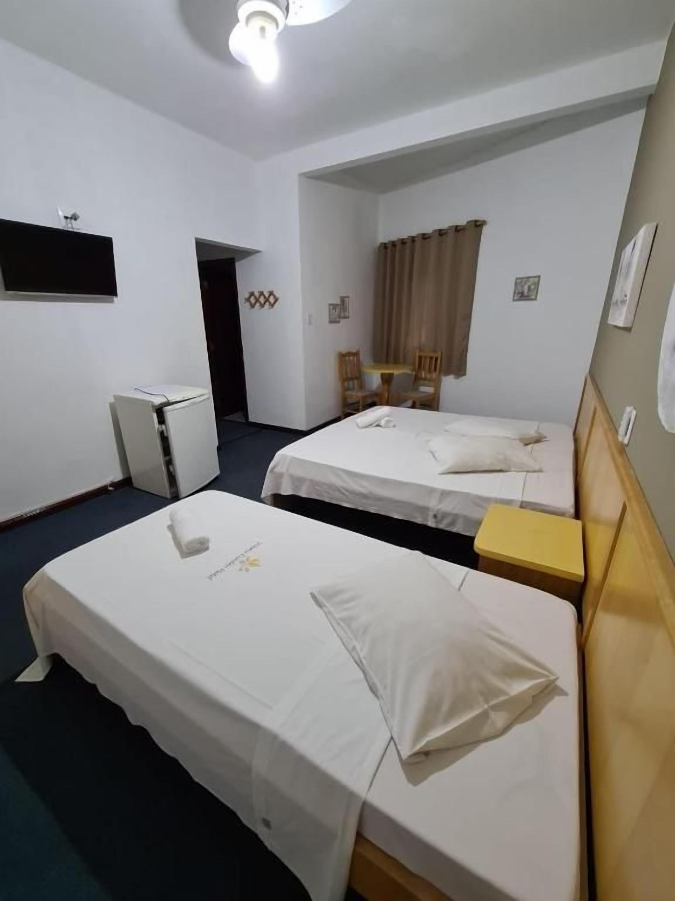 Une chambre d’hôtel avec deux lits, un bureau, une chaise, une petite table et un téléviseur fixé au mur.