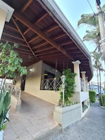 A covered outdoor area with a tiled floor, potted plants, and a wooden ceiling structure.