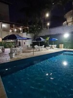 Una piscina con sillas de descanso y sombrillas, rodeada por un área pavimentada con plantas en macetas.