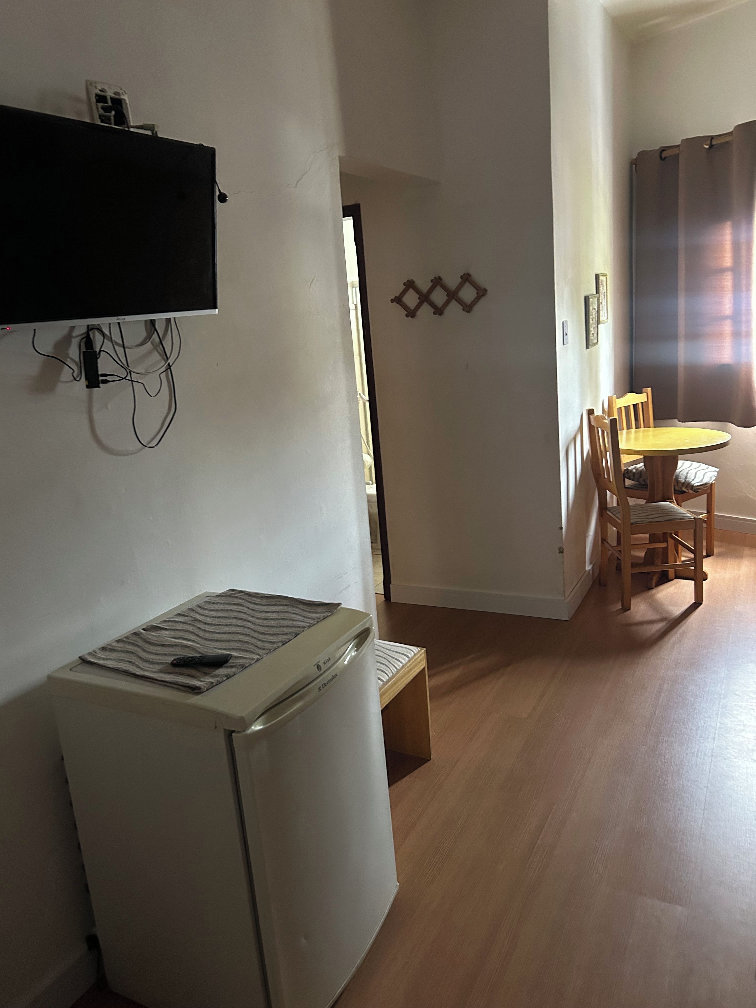 Un espace de vie compact comprenant un coin cuisine, un coin repas avec des chaises en bois et un téléviseur fixé au mur.