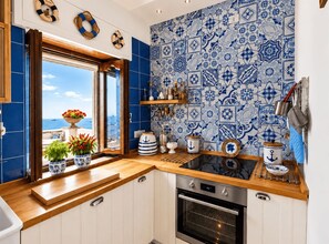 A kitchen with a view of the sea, blue and white patterned tiles, wooden countertops, and a stainless steel oven. - Rosa Tower | Sea View Villa · Step-Free · Private Parking · Sun Deck (Praiano)
