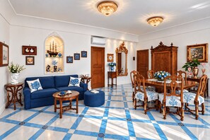 Ein Zimmer mit einem blauen Sofa, einem Holzesstisch mit Stühlen, einem gemusterten Boden und Wandleuchten.