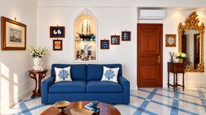 A living room with a blue sofa, decorative wall art, and a tiled floor. - Rosa Tower | Sea View Villa · Step-Free · Private Parking · Sun Deck (Praiano)