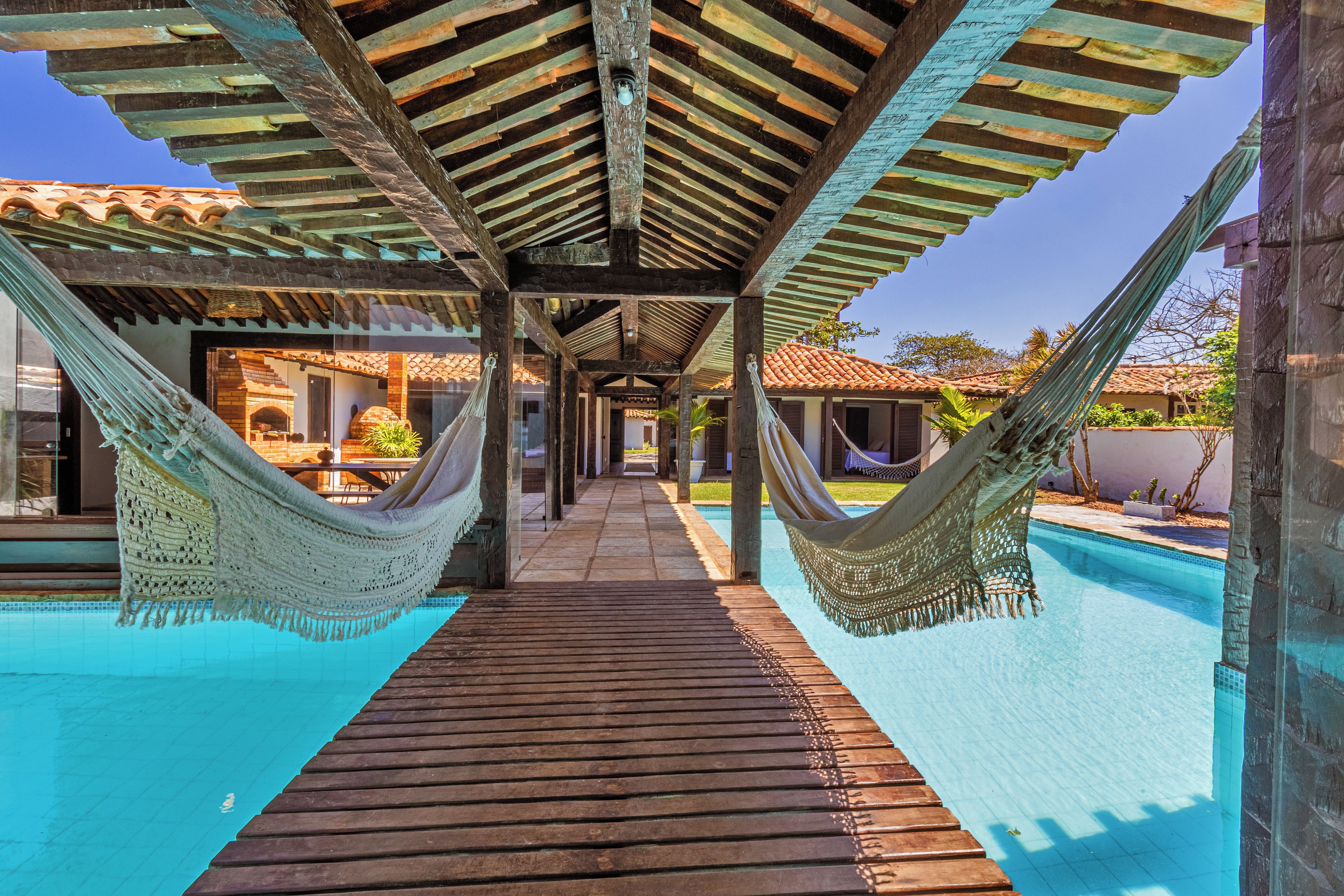Une terrasse en bois mène à une piscine, de chaque côté de laquelle sont disposés des hamacs.