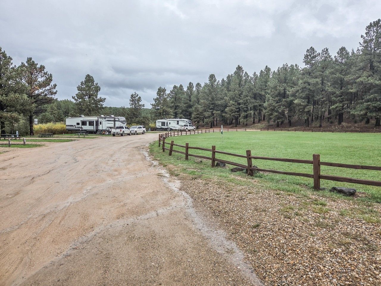 A dirt road leading to a fenced campground with RVs parked.