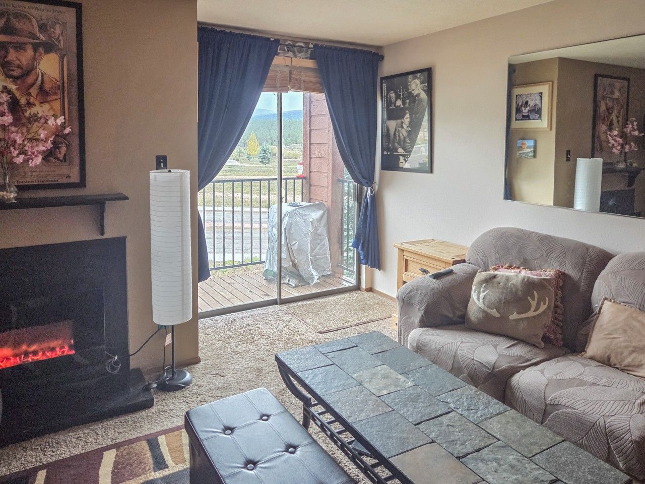 Ein Wohnzimmer mit Kamin, einer Couch, einem Couchtisch und Blick durch eine Glastür auf eine Terrasse.