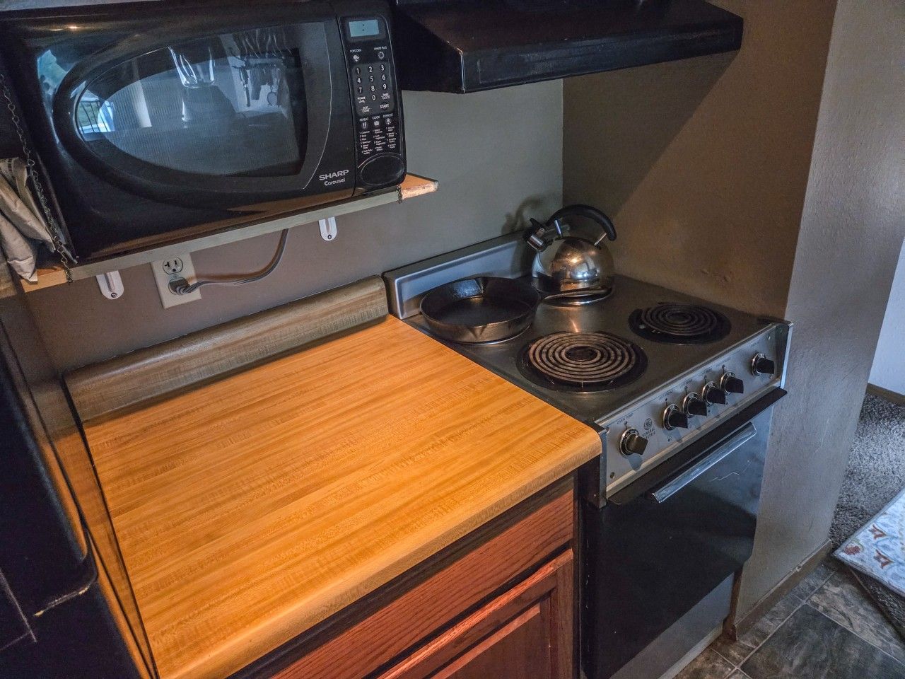 A compact kitchen with a microwave, kettle, stove, and oven.