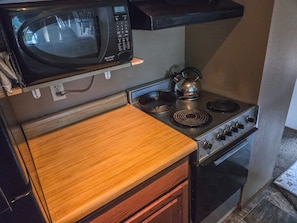 Een kleine keuken met een magnetron, waterkoker, fornuis en oven.