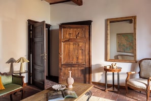 A room with a wooden door, a round table with books, a chair, a lamp, and a framed map on the wall. - Comfort and relaxation in the heart of the Crete Senesi (Toscana)