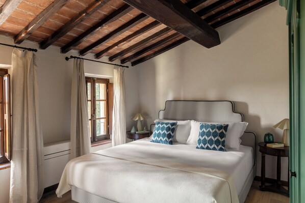 A bedroom with a bed, a nightstand, a lamp, and a window with curtains. - Comfort and relaxation in the heart of the Crete Senesi (Toscana)