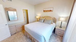 A bedroom with a large bed, two bedside tables with lamps, a mirror, and a door. - Sandpiper Cove 9127 1 Bedroom Condo (Destin)