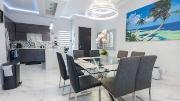 A modern dining area with a glass table, black and grey chairs, and a painting of a beach scene.