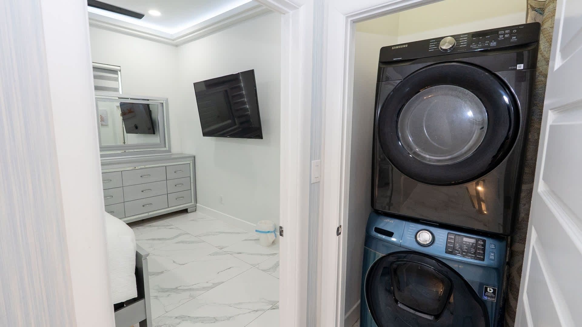 Une buanderie équipée d’un lave-linge et d’un sèche-linge à chargement frontal, d  ’un meuble gris et d’un téléviseur fixé au mur.