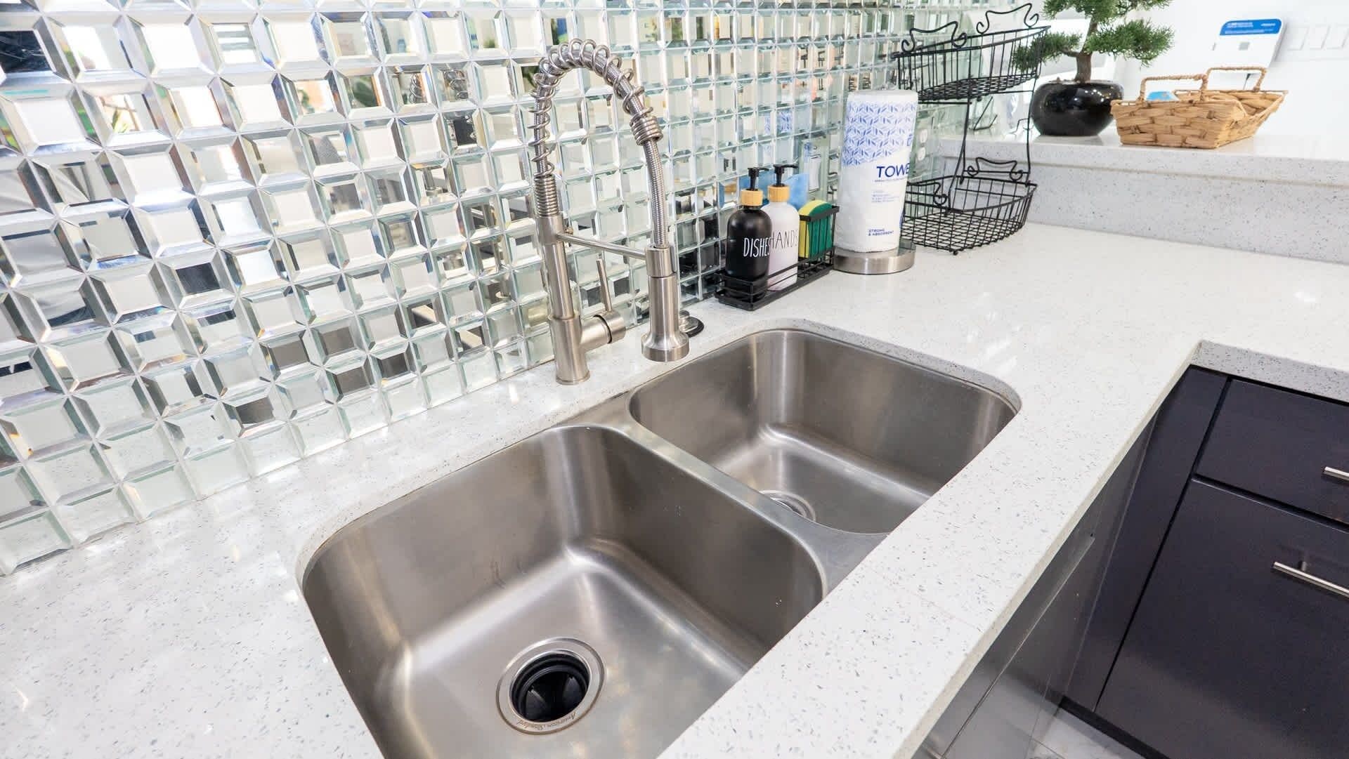 A kitchen with a double stainless steel sink, a modern faucet, and a backsplash made of reflective tiles.