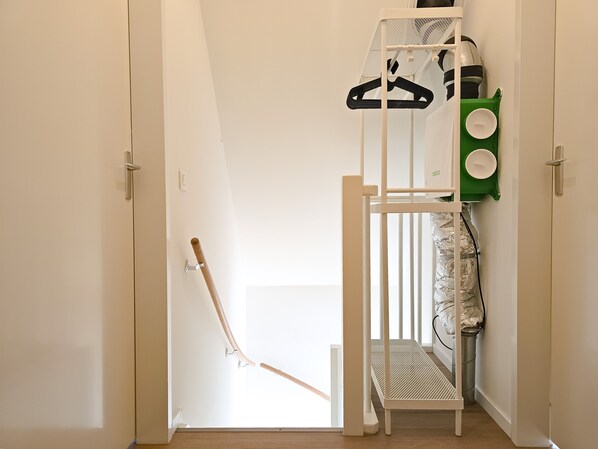 Ein Zimmer mit einer weißen Tür, einem Kleiderständer mit Kleiderbügeln, einem grünen Stauraum und einer weißen Bank.