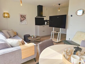 Ein modernes Wohnzimmer mit einer Couch, einem runden Couchtisch, einem Fernseher und einer Küchenzeile.
