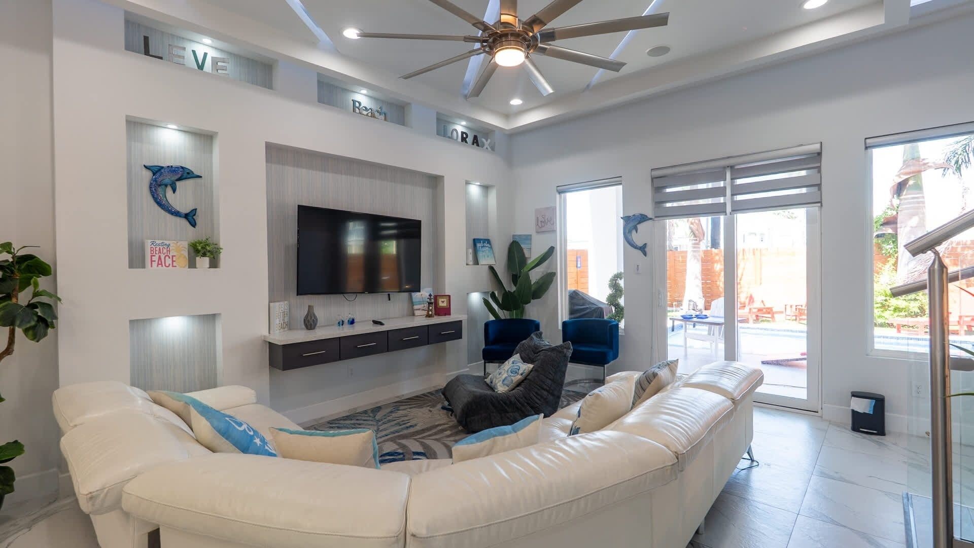 Ein modernes Wohnzimmer mit einem großen weißen Sofa, einem Flachbildfernseher und einem Deckenventilator.