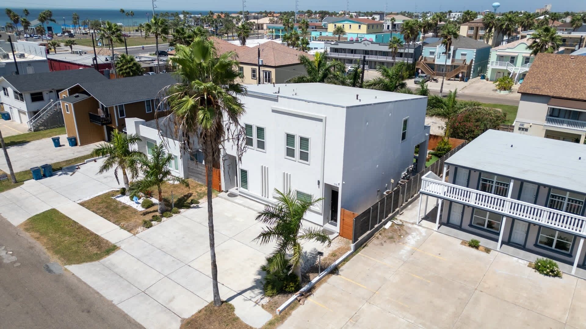 A residential area with a modern two-story house, a balcony, and a view of the ocean.