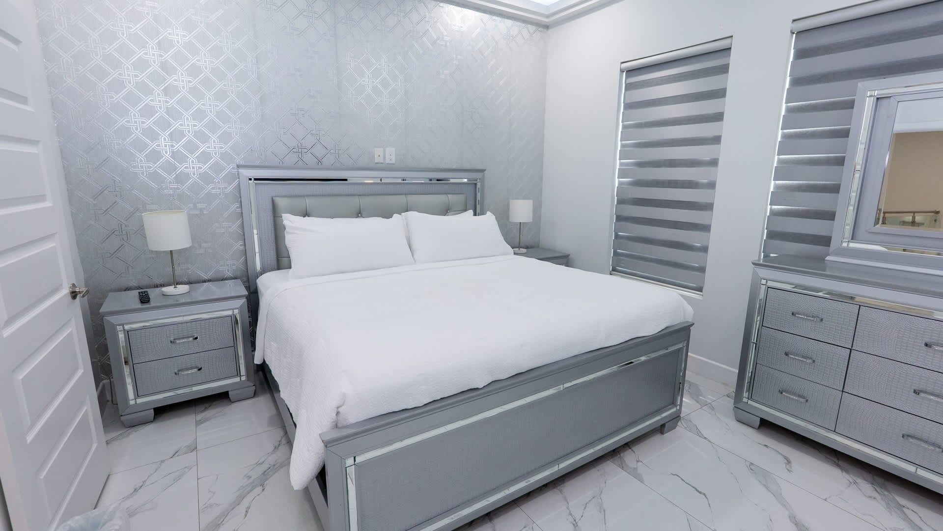 Een slaapkamer met een bed, nachtkastjes, een dressoir en een raam met zonwering.