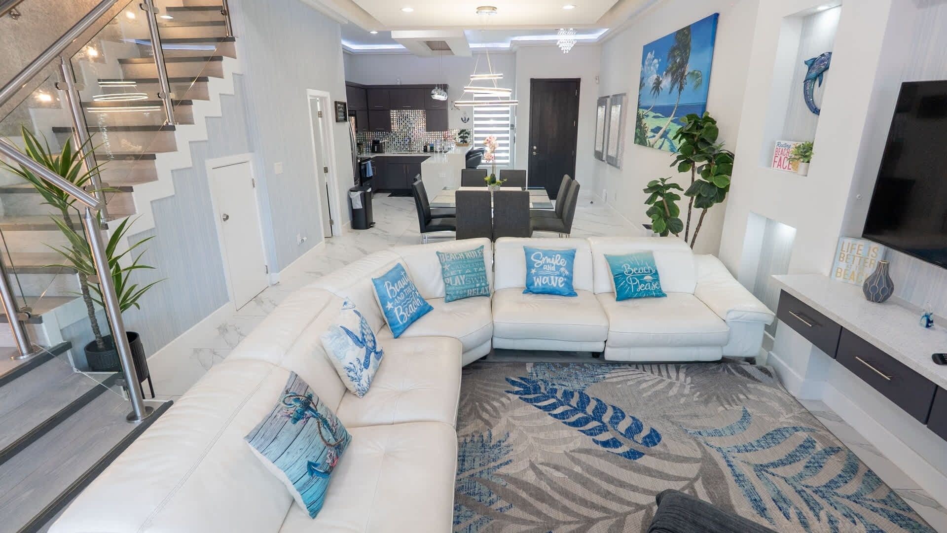 A modern living room with a sectional sofa, a staircase, and a kitchen in the background.