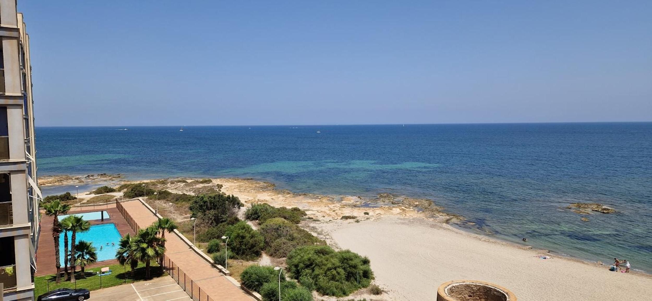 Blick auf die Küste mit Strand, klarem blauen Meer und einem Schwimmbad.