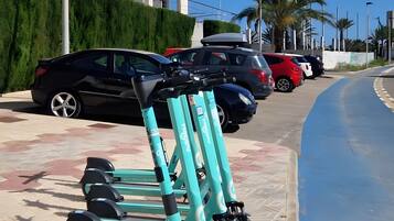 Un espace de stationnement avec plusieurs trottinettes électriques, une rangée de voitures garées et un immeuble doté de nombreux balcons.