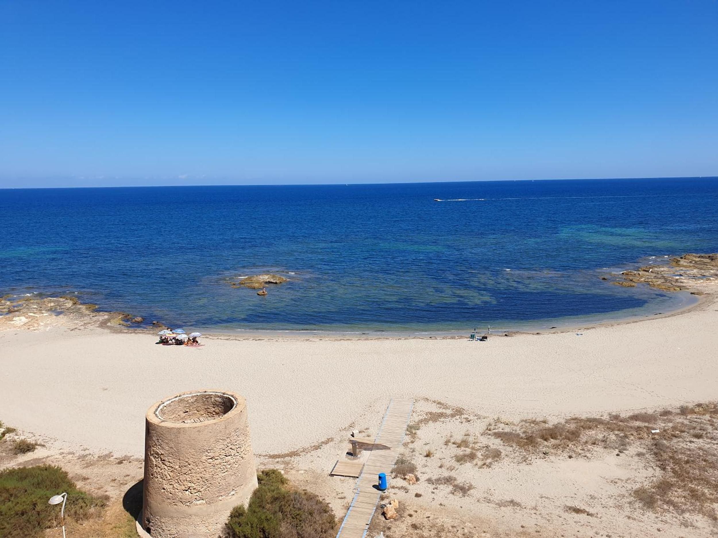 A beach with clear blue water, a sandy shore, and a stone structure.