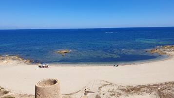A beach with clear blue water, a sandy shore, and a stone structure.