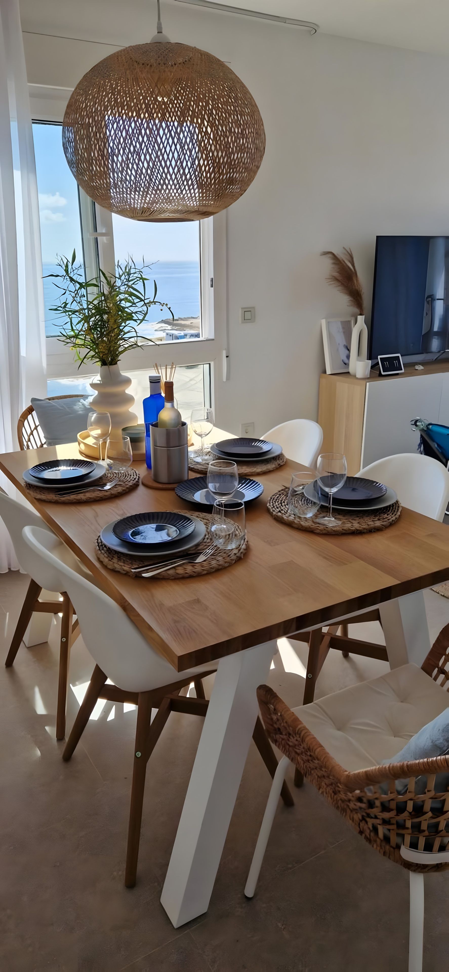 Un coin repas avec une table en bois dressée pour quatre personnes, entourée de chaises blanches.