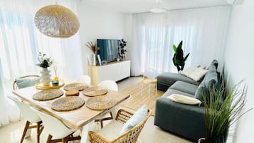 A modern living room with a dining area, featuring a sofa, a TV, and a dining table with chairs.