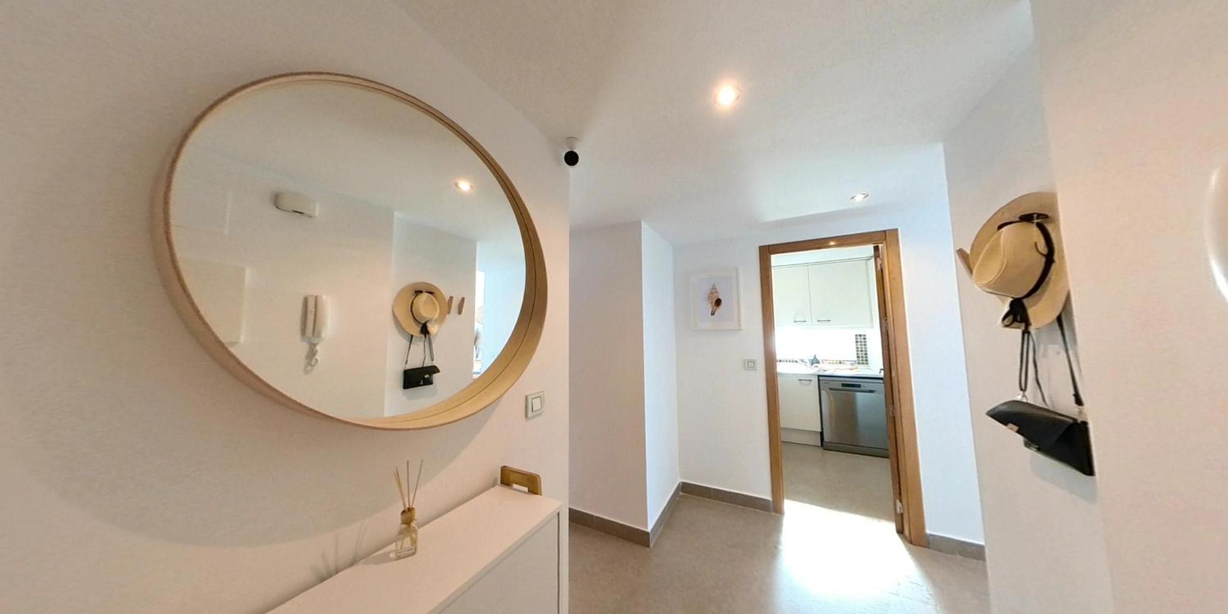 Un couloir avec un grand miroir, un porte-chapeaux fixé au mur et une porte donnant sur un espace cuisine.
