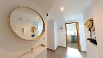 Un couloir avec un grand miroir, un porte-chapeaux fixé au mur et une porte donnant sur un espace cuisine.
