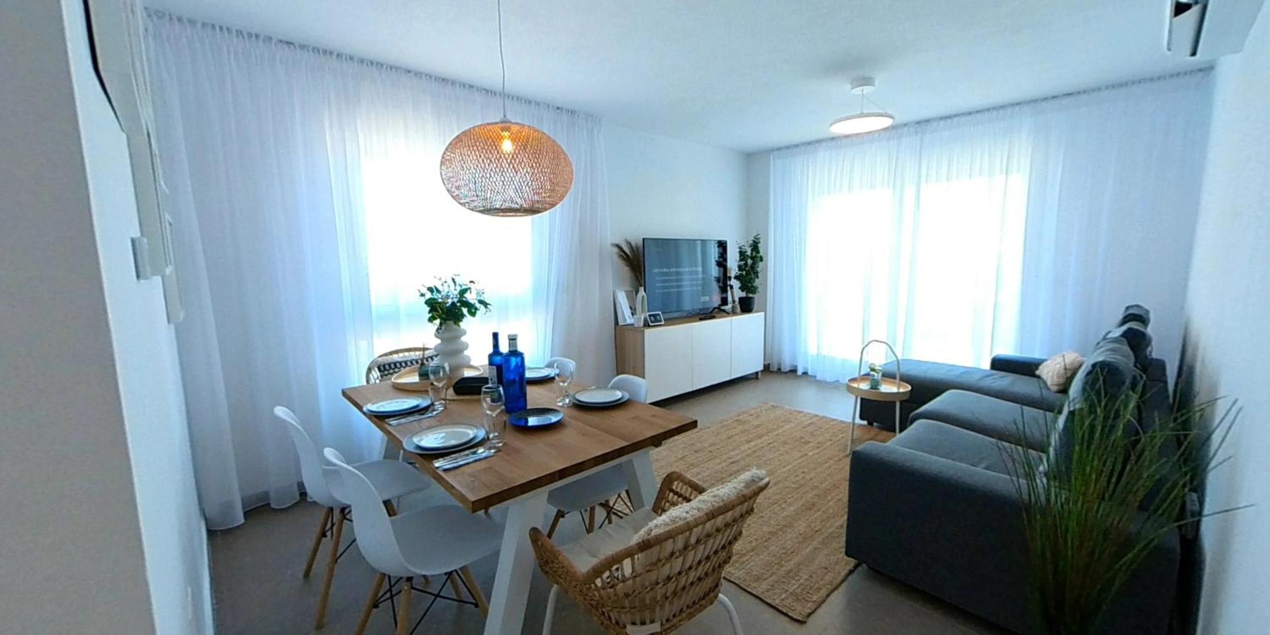 Ein modernes Wohnzimmer mit Essbereich, einer Couch, einem Fernseher und einem großen Fenster mit Vorhängen.