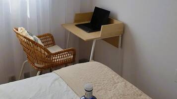 Une chambre d’hôtel avec un lit, un bureau avec un ordinateur portable, une chaise en osier et un plateau avec une bouteille et des verres.
