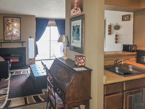 A living room with a fireplace, a wooden bench, and a kitchen area with a sink and toaster.