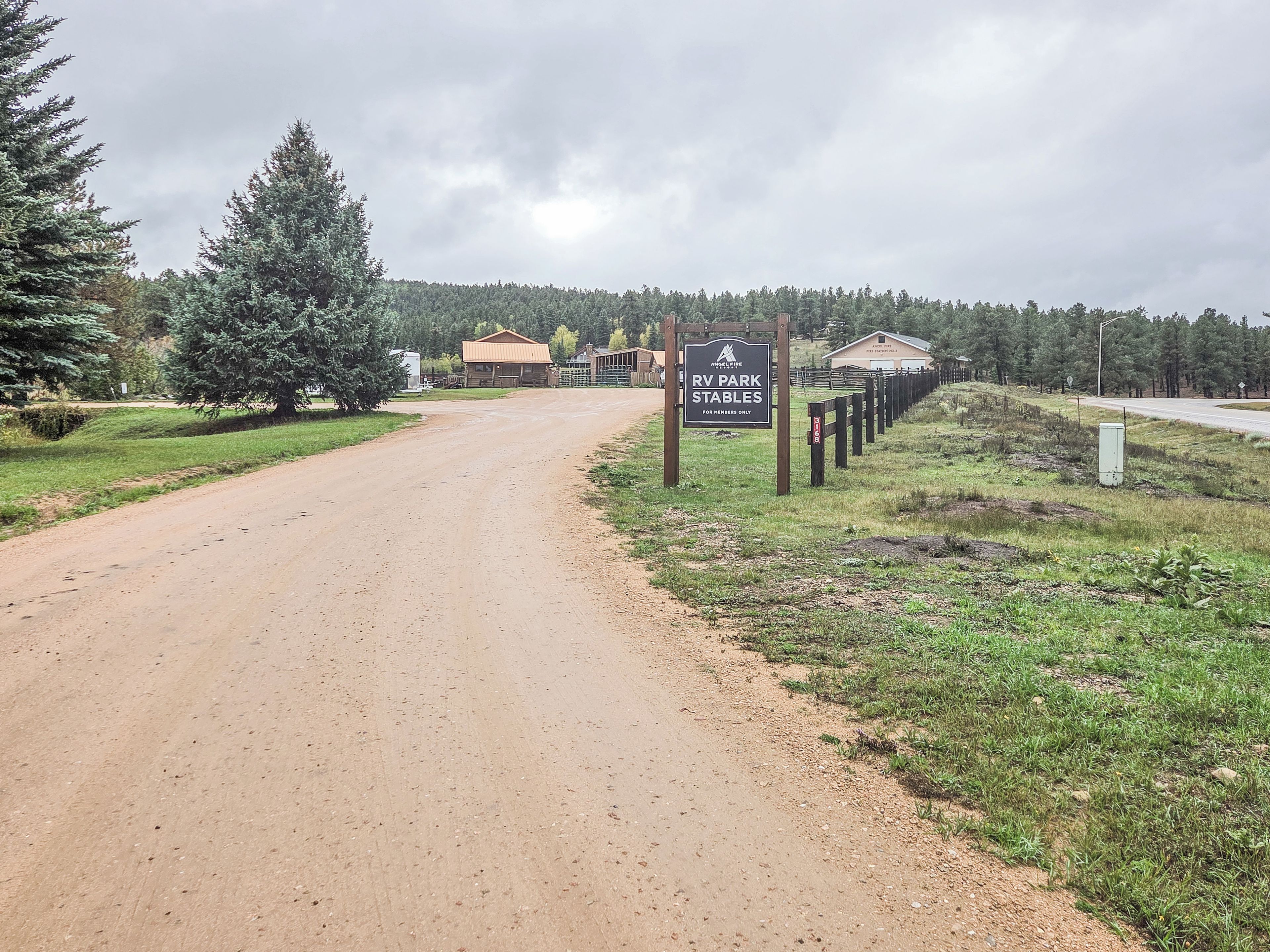 Ein Feldweg führt zu einem Schild für den RV-Park und die Stallungen, umgeben von Bäumen und einem Gebäude im Hintergrund.