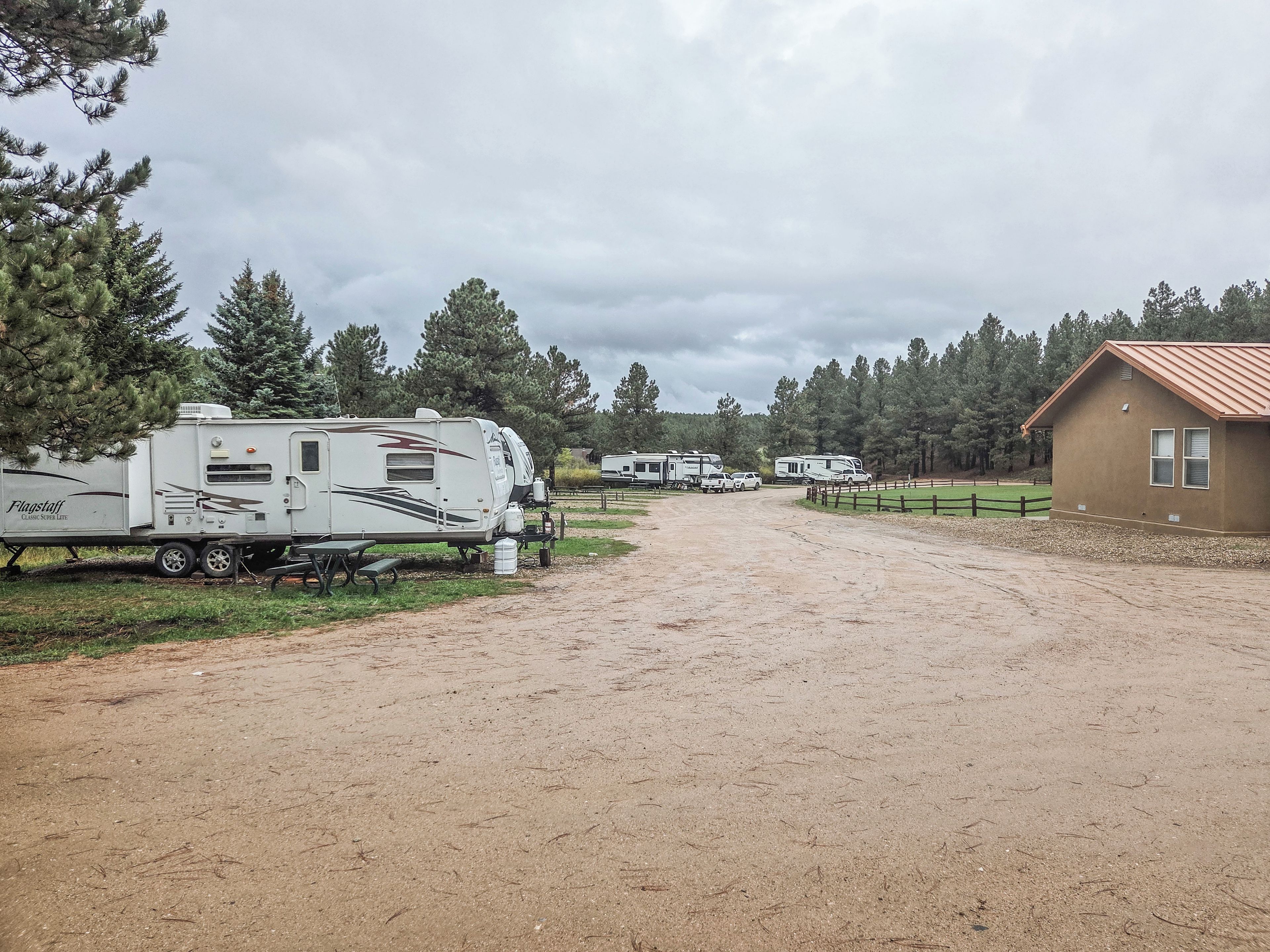 A gravel driveway leading to a row of RVs parked beside a building with a brown roof.