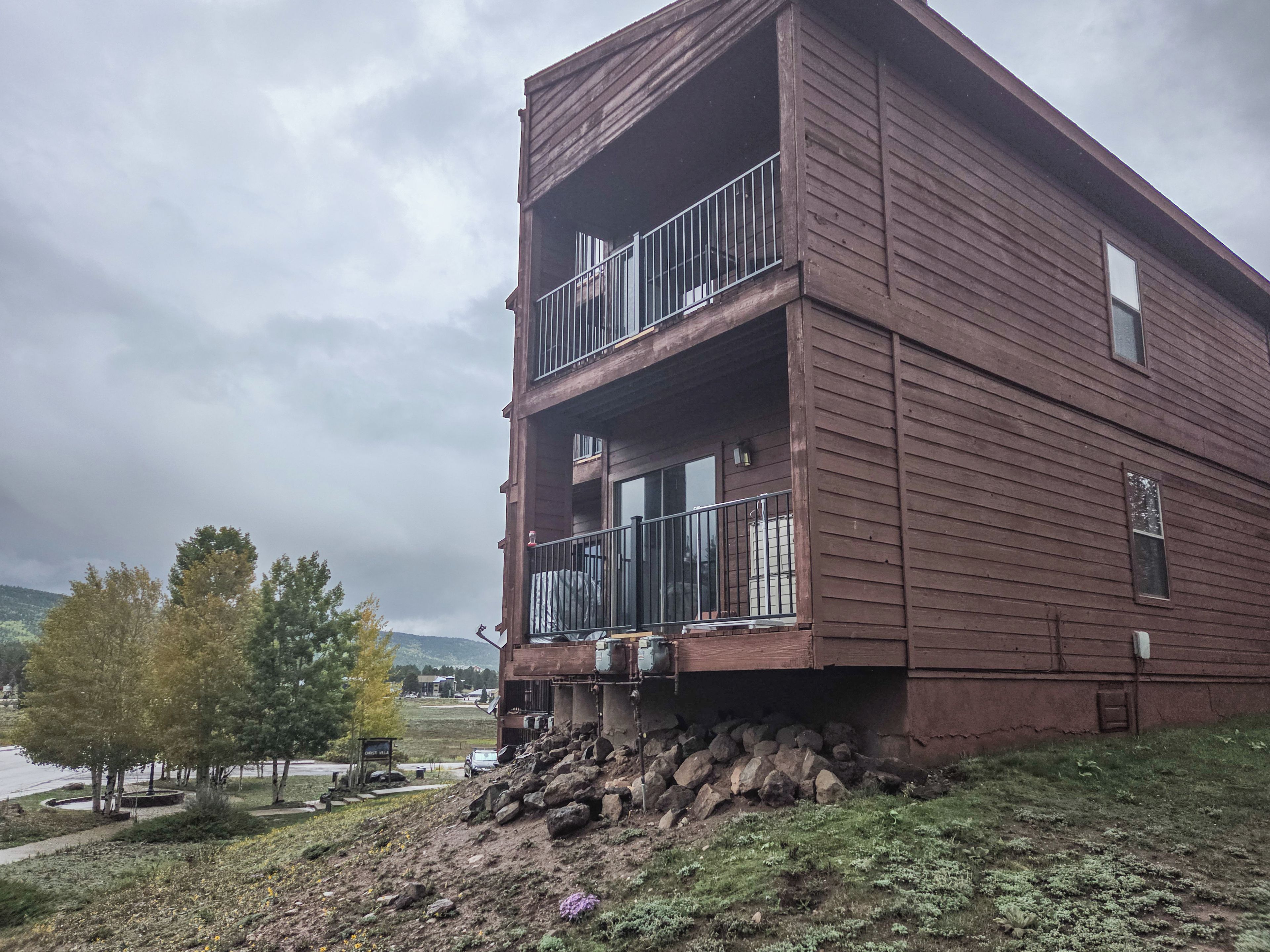 Edificio de madera de dos pisos con balcones, un pequeño jardín y vistas del paisaje circundante.